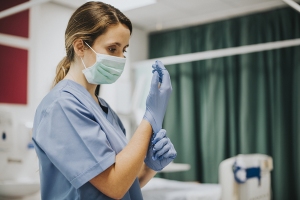 Hygiene in Pflegeberufen Krankenpflegerin mit OP-Maske zieht sich Gummihandschuhe an